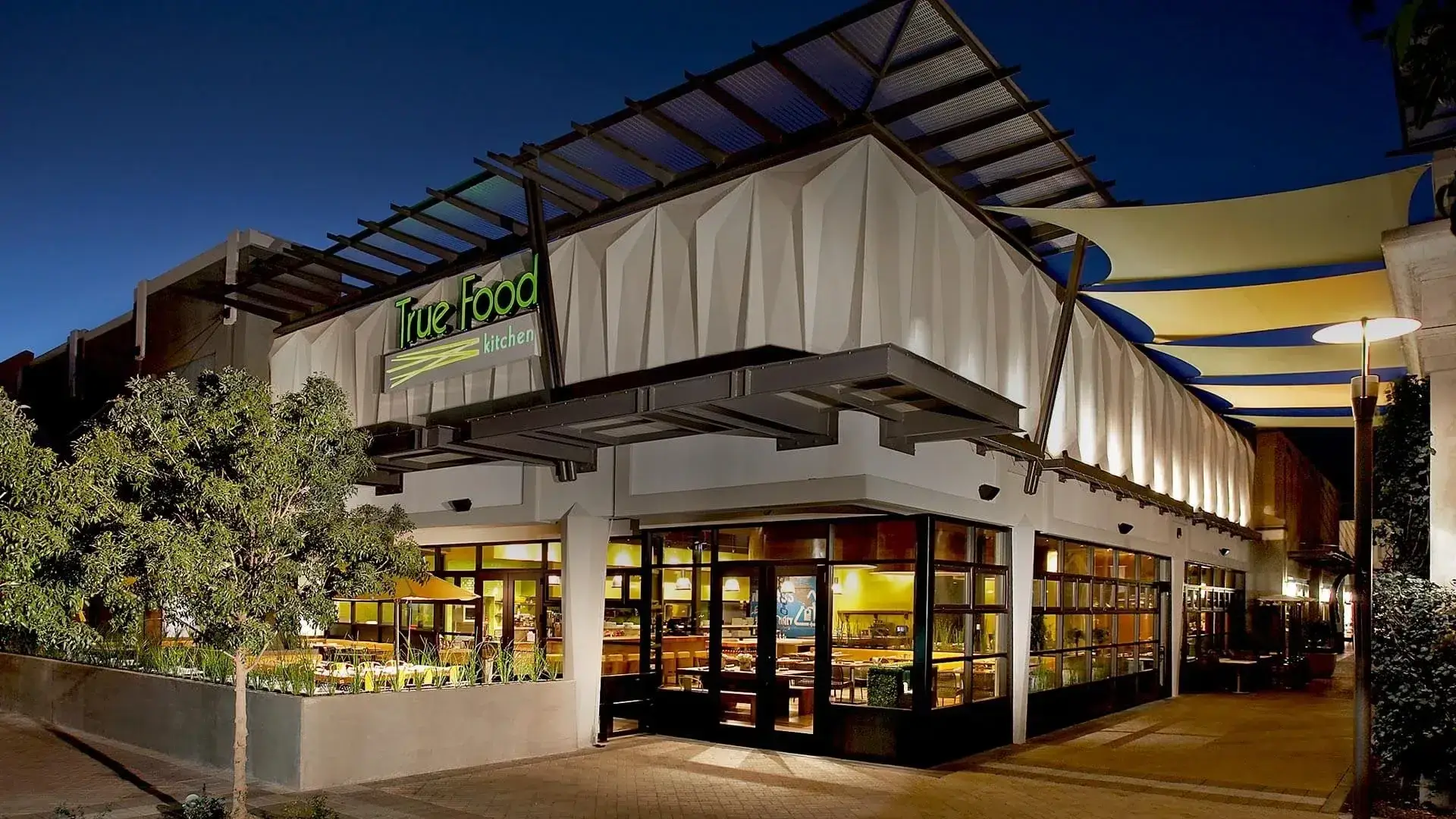 True Food Kitchen at Scottsdale Quarter photographed at dusk, its dining room lit through floor to ceiling windows under a tented roof.