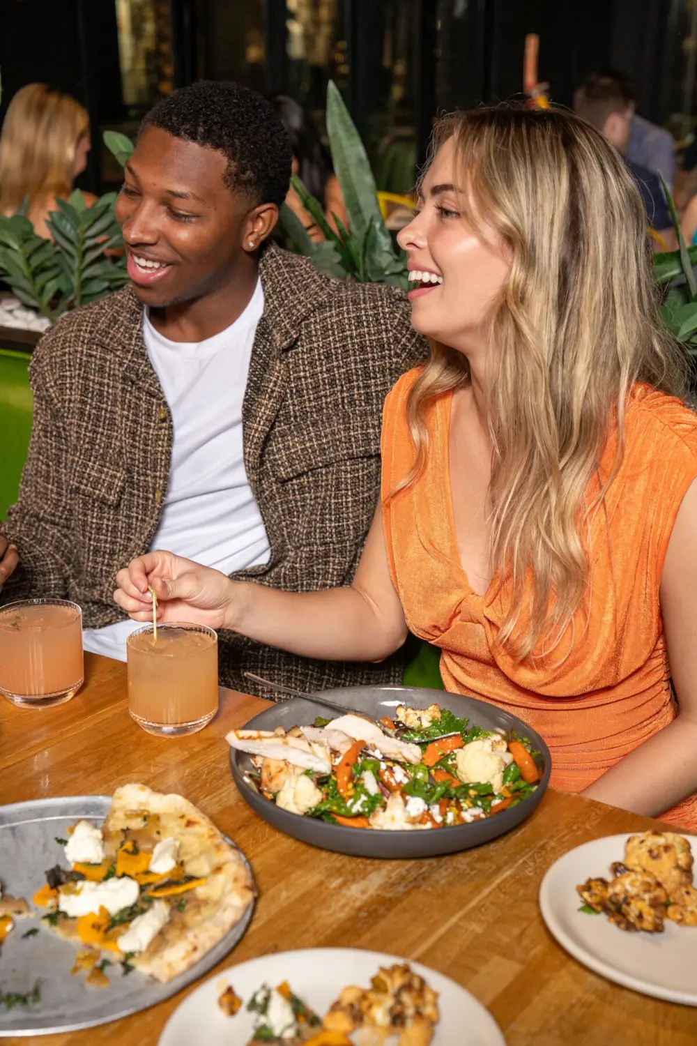 Two guests seated at a True Food Kitchen table with cocktails and a shared dish between them.